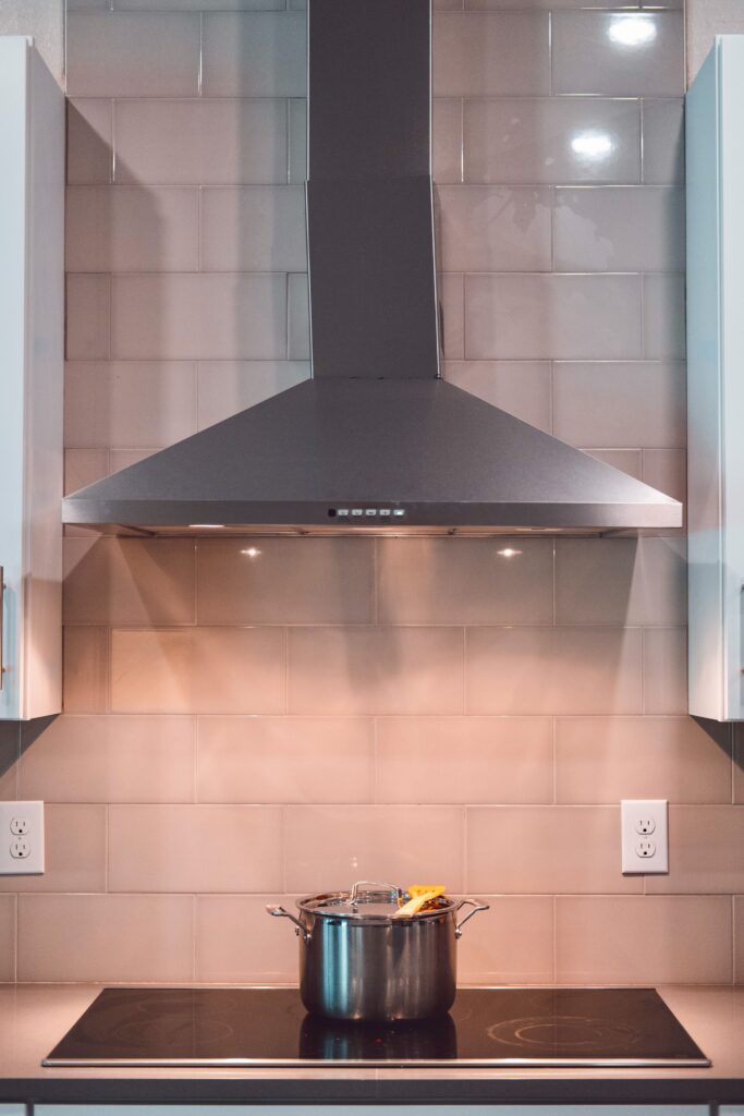 A contemporary kitchen scene featuring a stainless steel exhaust hood and a pot on the stove.